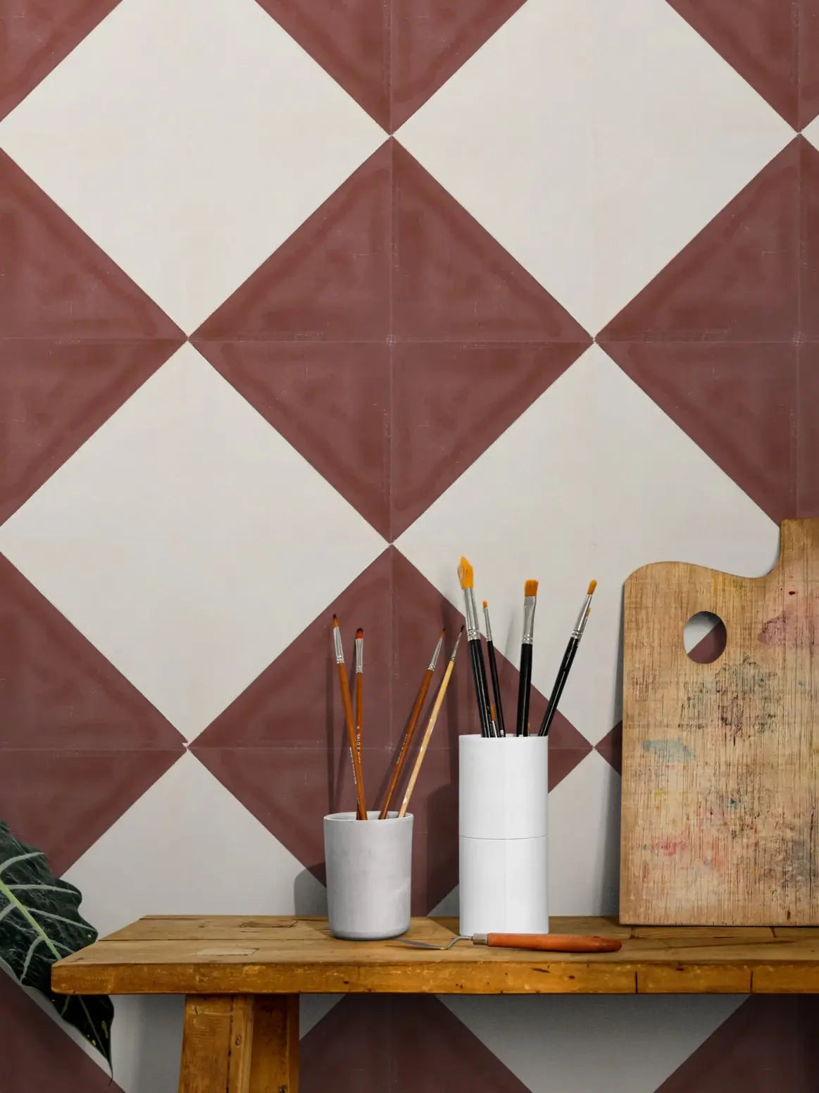Baldosa hidráulica-Mosaico tapiz en una pared blanca y roja junto a utensilios de pintura.